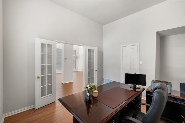 home office with french doors, visible vents, a high ceiling, light wood-style floors, and baseboards