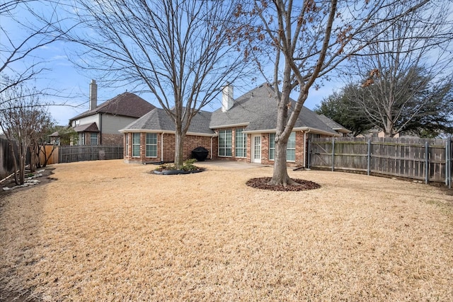 rear view of property with a lawn, a fenced backyard, a chimney, a patio area, and brick siding