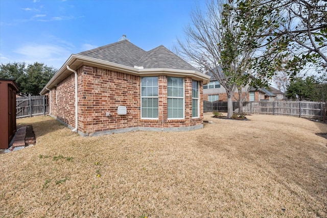 rear view of house with a shingled roof, brick siding, a lawn, and a fenced backyard