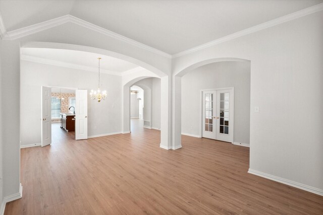 spare room with french doors, light wood-style flooring, ornamental molding, a chandelier, and baseboards