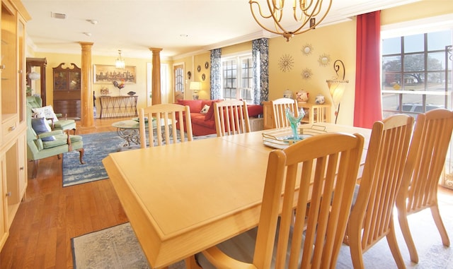 dining room featuring crown molding, visible vents, an inviting chandelier, wood finished floors, and ornate columns