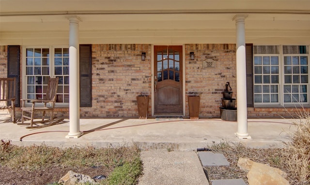 doorway to property with covered porch and brick siding