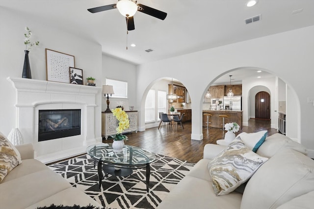 living room with visible vents, recessed lighting, arched walkways, a tile fireplace, and dark wood-type flooring