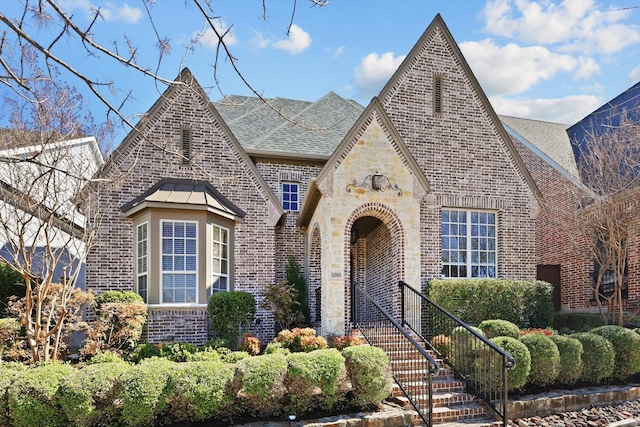 tudor house with stone siding, brick siding, and roof with shingles