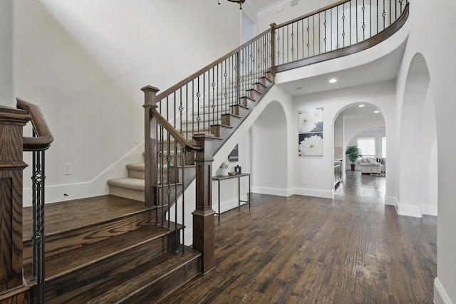 staircase featuring baseboards, recessed lighting, a high ceiling, wood finished floors, and arched walkways