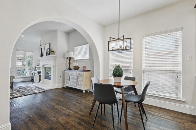 dining space with dark wood finished floors, a glass covered fireplace, baseboards, and a chandelier