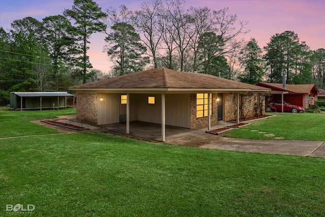 back of house at dusk featuring brick siding and a lawn