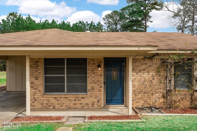 doorway to property with board and batten siding, brick siding, and a shingled roof