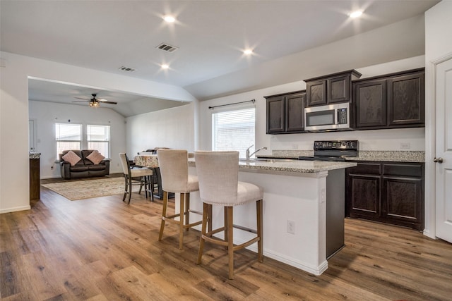 kitchen featuring visible vents, lofted ceiling, stainless steel microwave, a kitchen breakfast bar, and black range with electric cooktop