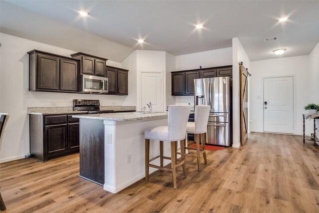 kitchen featuring light wood finished floors, stainless steel appliances, visible vents, dark brown cabinetry, and a kitchen bar