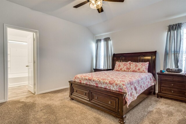 bedroom with lofted ceiling, light colored carpet, a ceiling fan, ensuite bath, and baseboards