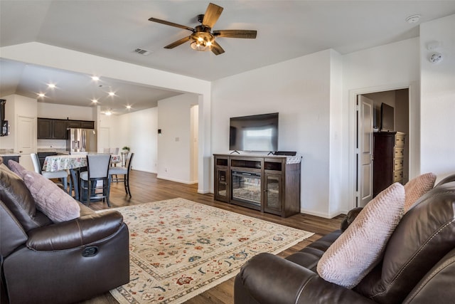 living room with baseboards, visible vents, ceiling fan, dark wood-type flooring, and vaulted ceiling