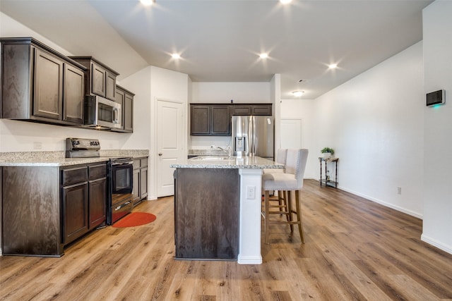 kitchen with dark brown cabinets, appliances with stainless steel finishes, light wood-style flooring, and a kitchen breakfast bar