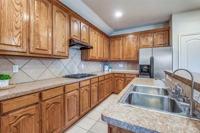 kitchen featuring under cabinet range hood, brown cabinets, stainless steel fridge, gas cooktop, and a sink