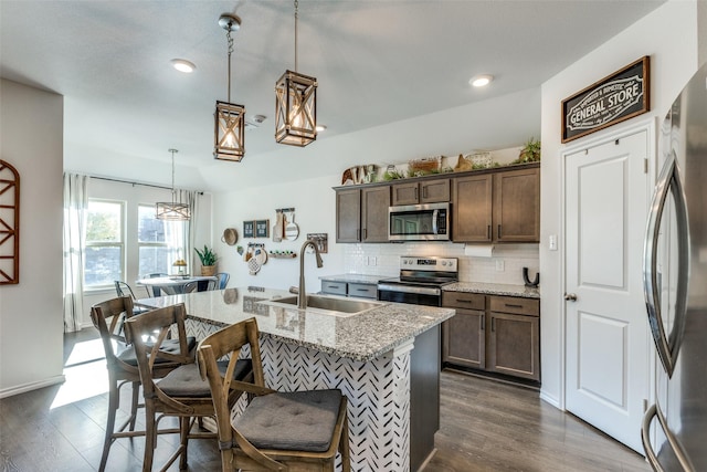 kitchen with a sink, appliances with stainless steel finishes, decorative backsplash, dark wood-style floors, and a kitchen bar