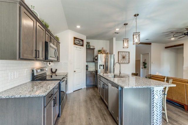 kitchen with stainless steel appliances, a breakfast bar, a sink, open floor plan, and dark wood finished floors