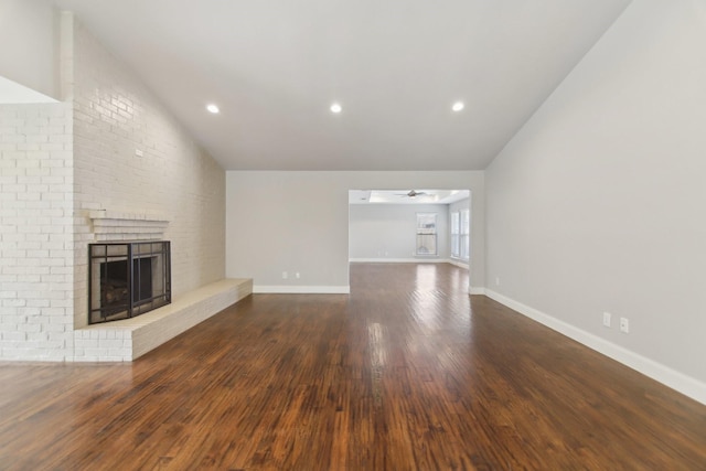 unfurnished living room featuring vaulted ceiling, a brick fireplace, wood finished floors, and a ceiling fan