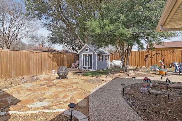 view of patio featuring an outbuilding, a fenced backyard, a fire pit, and a storage unit