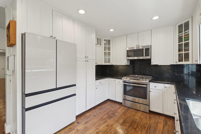 kitchen with white cabinets, glass insert cabinets, dark wood-style flooring, stainless steel appliances, and backsplash