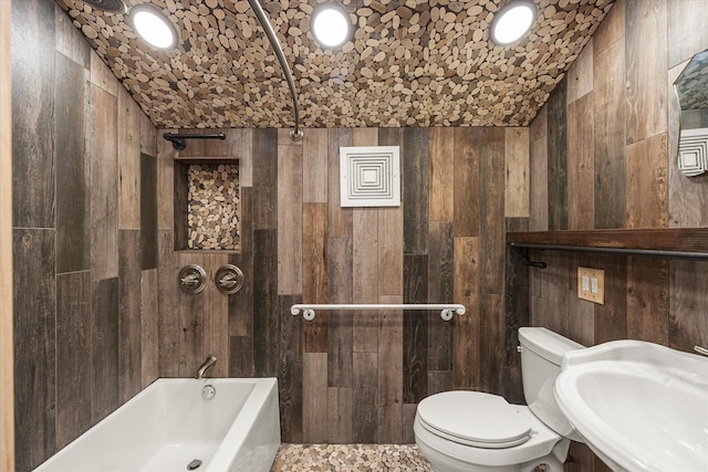 full bath with toilet, wood walls, washtub / shower combination, and a sink