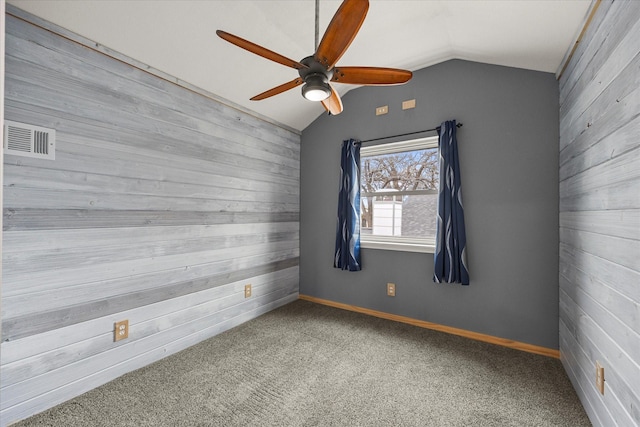 spare room with vaulted ceiling, wood walls, carpet, and visible vents