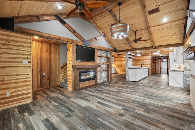 unfurnished living room featuring a ceiling fan, a glass covered fireplace, wood ceiling, beamed ceiling, and dark wood-type flooring