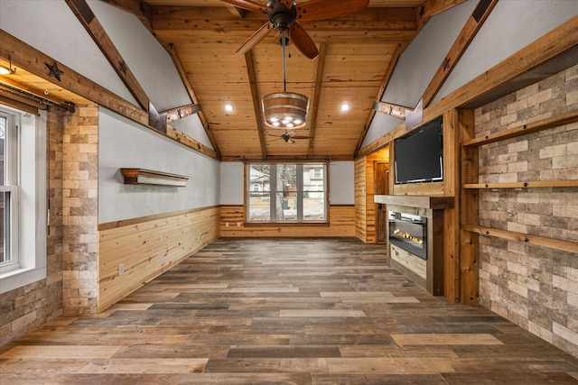 unfurnished living room with a wainscoted wall, a glass covered fireplace, dark wood-style flooring, and lofted ceiling