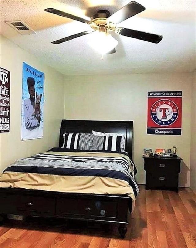 bedroom featuring a textured ceiling, wood finished floors, visible vents, and a ceiling fan