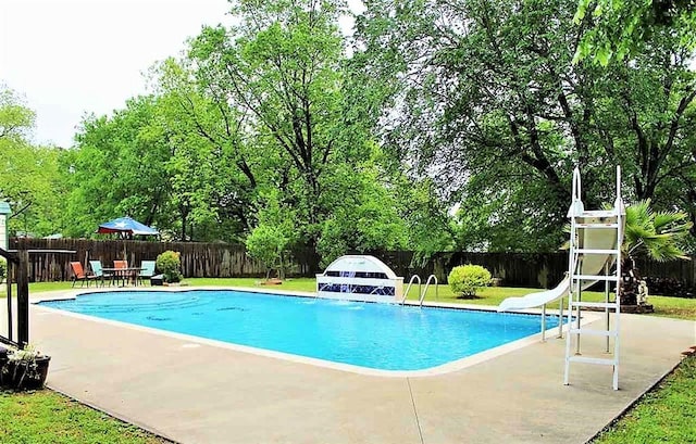 view of swimming pool featuring a fenced in pool, a lawn, a patio, a fenced backyard, and a water slide