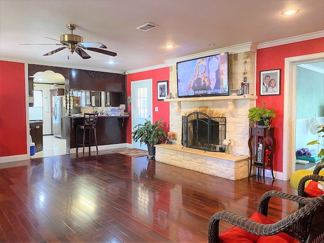 living room featuring visible vents, crown molding, a stone fireplace, and wood finished floors