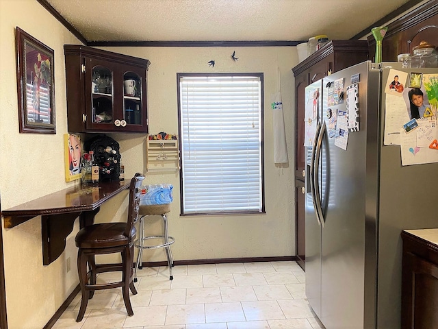 kitchen with a textured ceiling, dark brown cabinetry, ornamental molding, stainless steel fridge, and glass insert cabinets