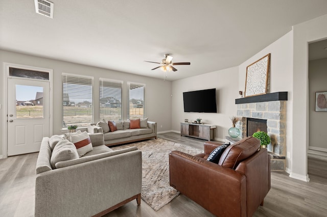 living room featuring a fireplace, wood finished floors, a ceiling fan, visible vents, and baseboards