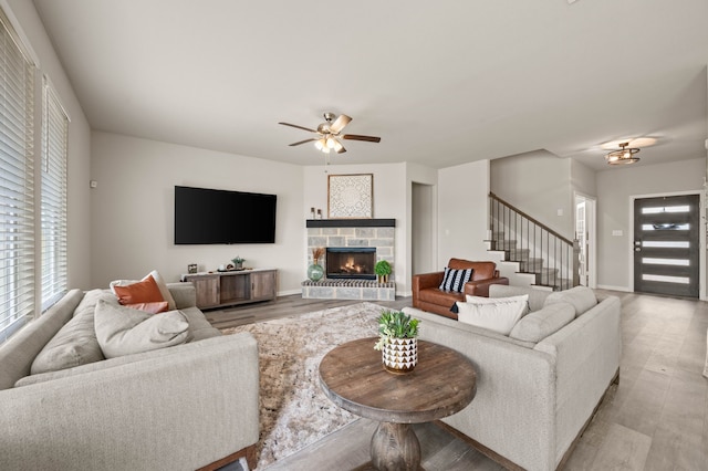 living area featuring a stone fireplace, a healthy amount of sunlight, ceiling fan, and light wood-style flooring