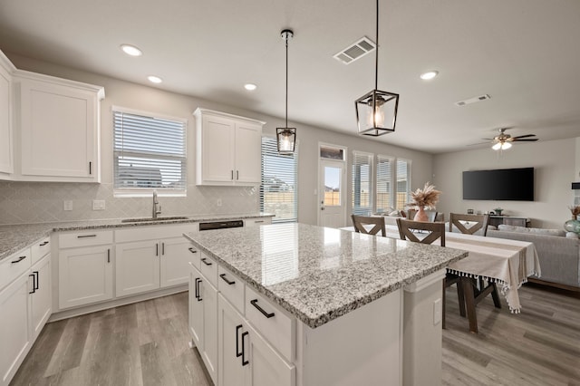 kitchen with light wood finished floors, visible vents, decorative backsplash, a kitchen island, and a sink