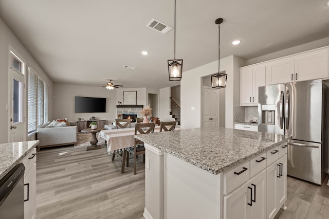 kitchen featuring stainless steel appliances, visible vents, backsplash, light wood-style flooring, and a stone fireplace