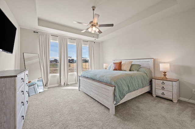 bedroom featuring baseboards, a raised ceiling, a ceiling fan, and light colored carpet