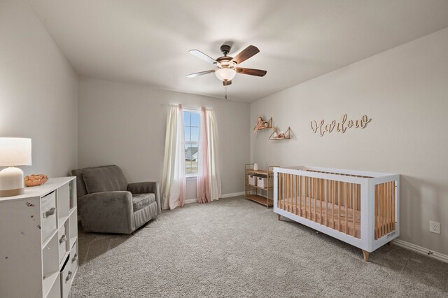 carpeted bedroom featuring a nursery area, a ceiling fan, and baseboards