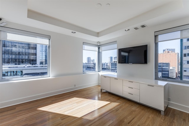 interior space with a tray ceiling, wood finished floors, visible vents, and baseboards