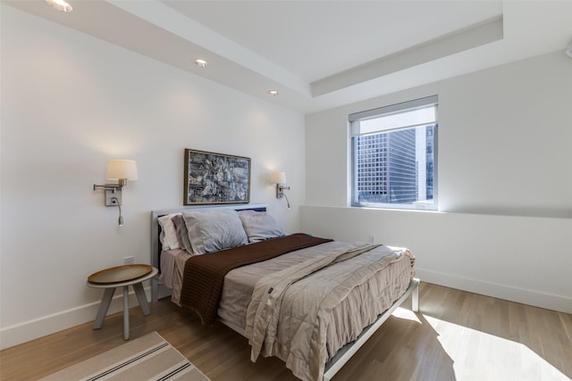 bedroom featuring baseboards, a tray ceiling, wood finished floors, and recessed lighting