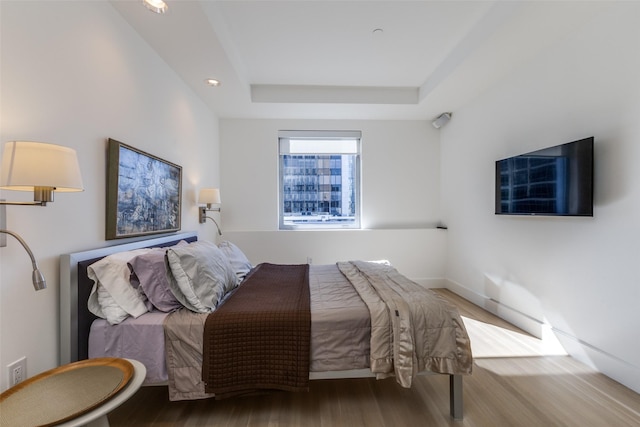 bedroom featuring wood finished floors, a raised ceiling, and baseboards