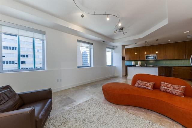 living area featuring a raised ceiling, rail lighting, and baseboards