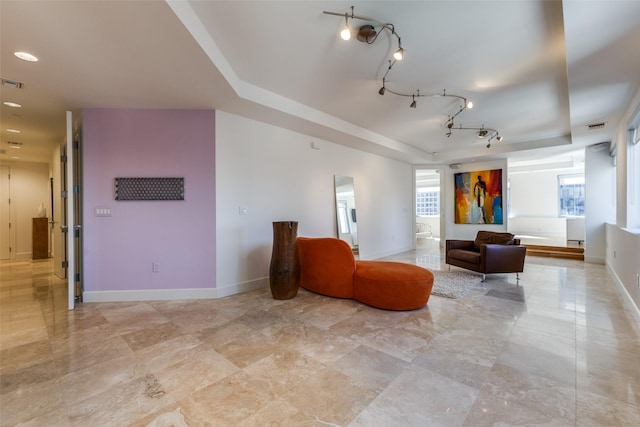 interior space featuring a tray ceiling, rail lighting, visible vents, and baseboards