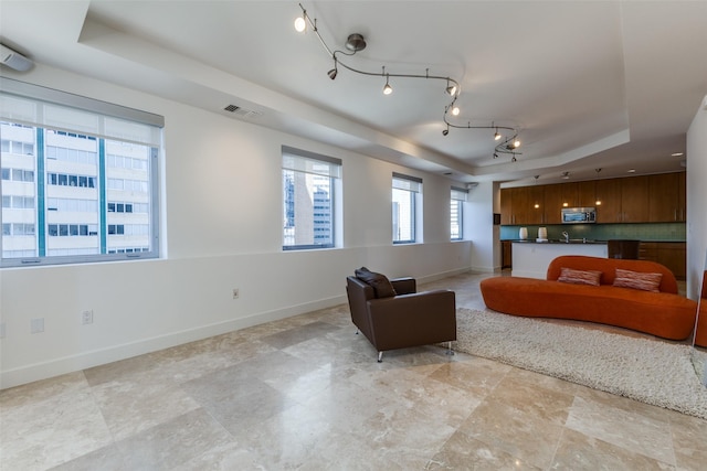 living area featuring track lighting, a tray ceiling, visible vents, and baseboards