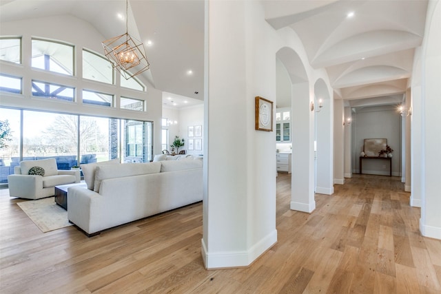 corridor with baseboards, light wood finished floors, high vaulted ceiling, arched walkways, and a chandelier