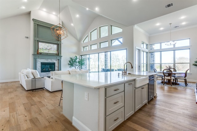 kitchen featuring visible vents, light wood finished floors, high vaulted ceiling, a sink, and a notable chandelier