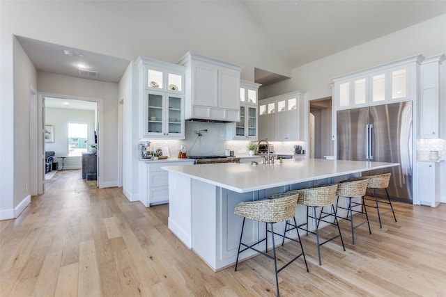 kitchen with light wood-type flooring, visible vents, stainless steel refrigerator, a spacious island, and white cabinets