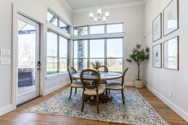 dining space with a notable chandelier, light wood-style floors, a high ceiling, crown molding, and baseboards