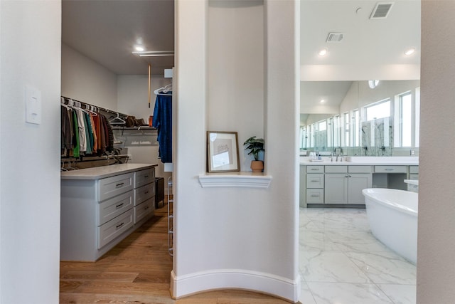 full bathroom featuring visible vents, a walk in closet, a soaking tub, marble finish floor, and vanity