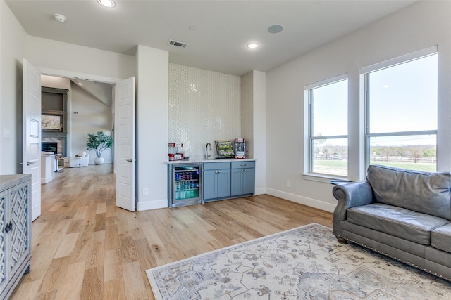 living area featuring indoor wet bar, light wood-style flooring, beverage cooler, and baseboards