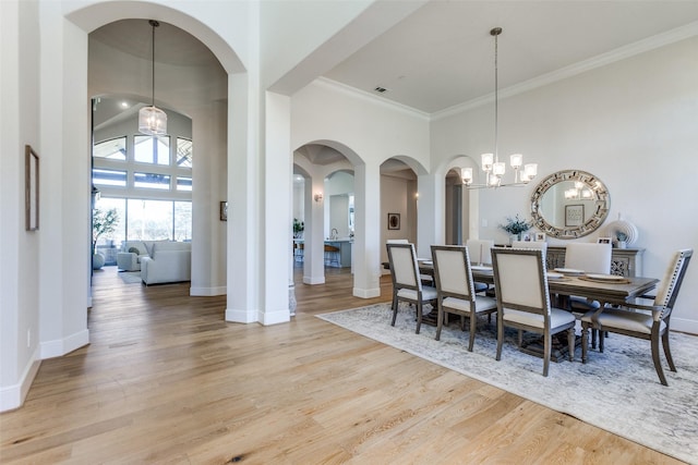 dining area featuring a notable chandelier, a high ceiling, ornamental molding, and light wood finished floors